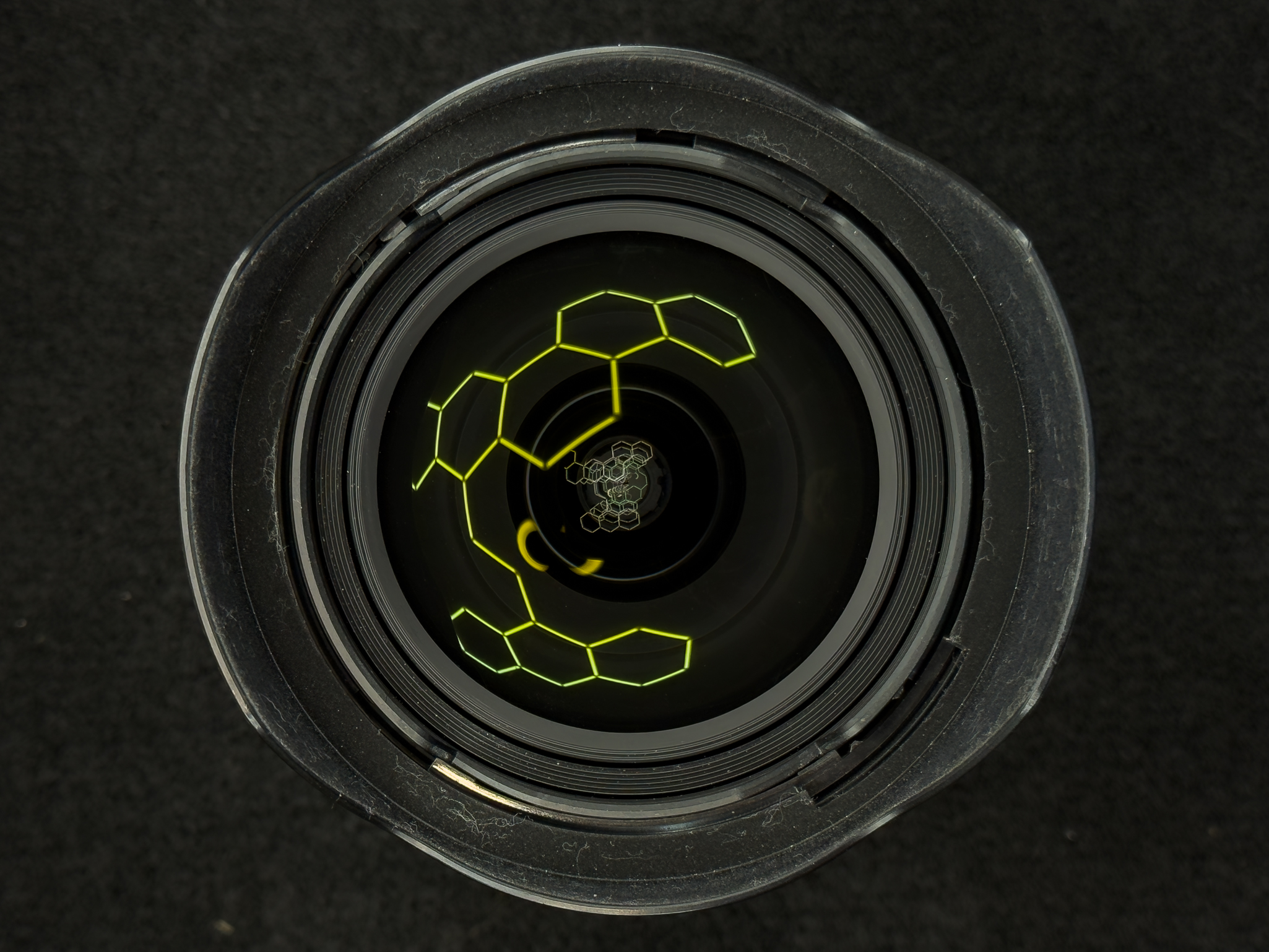Tight accent shot of the specialized bulbous front glass element catching a straight grid light to highlight the precise double-sided aspherical lens molding on the Nikon Z 14-24mm f/2.8 S
